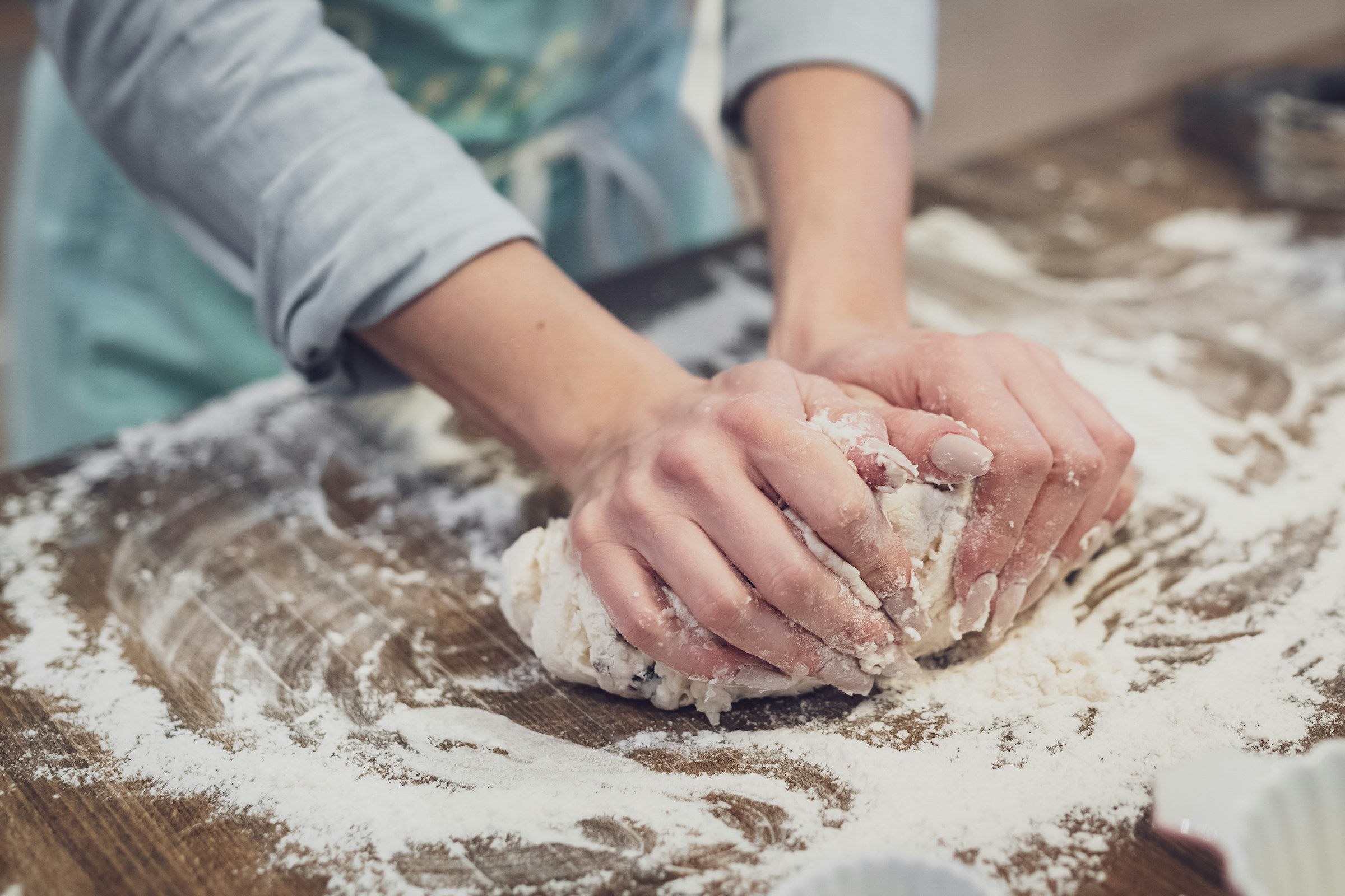 A baker in a blue apron kneading dough on a floured wood surface